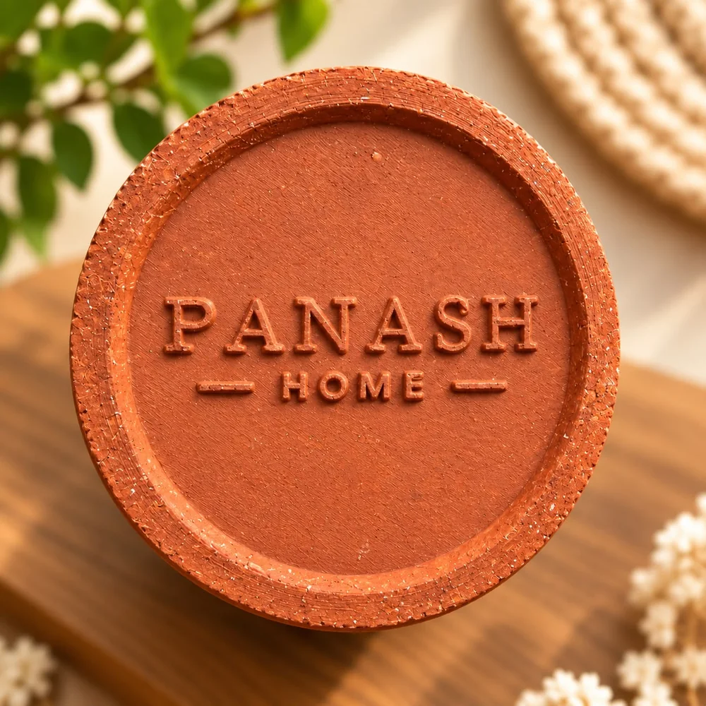 The underside of a terracotta diya with PANASH HOME raised in the clay.
