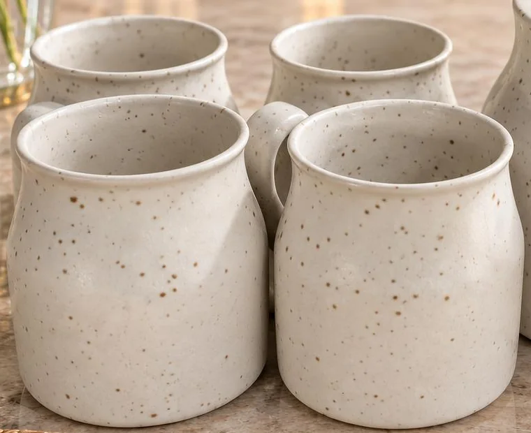 Four cream speckled cups standing together, with flared rims and rounded bodies.
